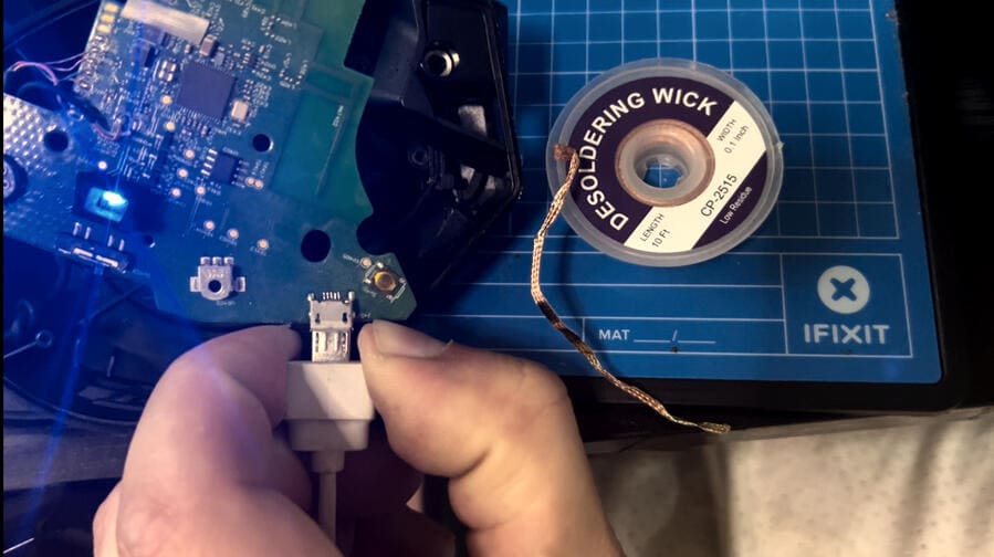 The same headset board after repair with a blue status LED lit and a micro-USB cable being fitted to the charging port.
